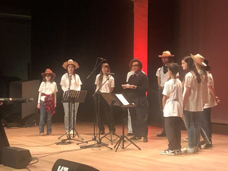 A group of 10 young people standing in a semi circle and singing on a stage
